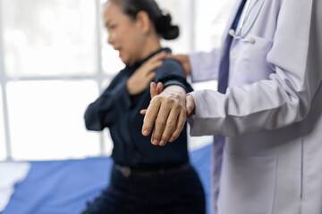 Senior woman suffering from shoulder and arm pain during medical examination with professional doctor in white coat holding her arm and shoulder, providing support and assessing range of motion.