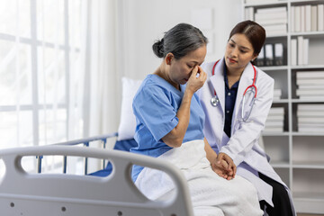 Young female doctor comforting a sad senior patient sitting on a hospital bed, expressing empathy...