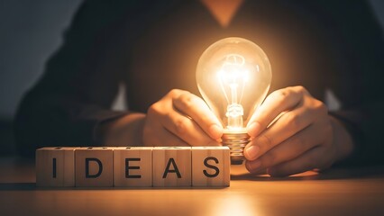 Hands Holding a Glowing Lightbulb next to Wooden Blocks Spelling Ideas for Creative Business Inspiration and Strategic Innovation
