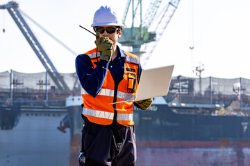 group of industrial engineers workers in a refinery - oil and gas processing equipment and machinery, engineers collaborate with a laptop, blueprint, and digital tablet at the oil storage tanks site.