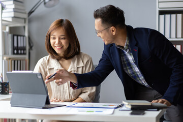 Two business people smiling and working together, analyzing financial chart using digital tablet and discussing new project strategy at office.