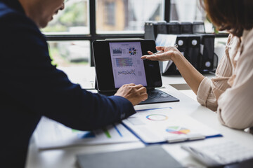 Business colleagues discussing financial data displayed on tablet and paperwork, collaborating on investment strategy, analyzing market trends and company performance in office.