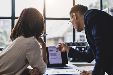 Business people analyzing financial charts and graphs on digital tablet and paperwork during corporate meeting.