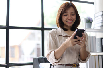 Young Asian businesswoman using smartphone and smiling in office.
