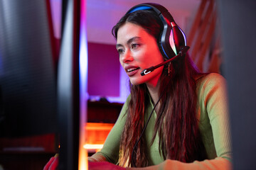 Focused female gamer with headset at computer desk setup