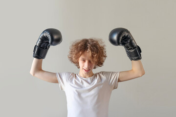 Determined Teenage Boy in Boxing Gloves Raising Hands in Victory Gesture. Authentic Concept of Inner Strength, Overcoming Challenges, Mental Resilience, and Youth Sports Motivation on Neutral Grey Bac