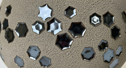 Close-up of a speckled ceramic surface adorned with numerous, glistening, six-sided, dark shapes. They have a reflective, silvery border
