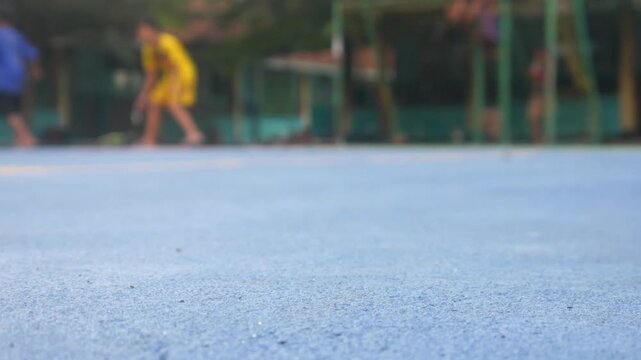 Boys are having fun playing soccer on a green school field with trees and school buildings in the background. Low focus on the texture of the field with a bokeh (blur) effect on the subject.