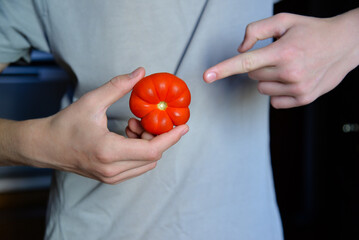 Man holding a red fresh tomato. Hand points to a tomato. Healthy eating