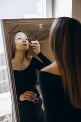 Young woman applying mascara and looking into the mirror