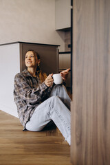 Woman sitting on floor at her kitchen and drinking coffee
