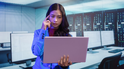 Serious Asian woman works on laptop while standing in high-tech workspace. digital tasks, data analysis, remote corporate connectivity, technology usage, data analysis, productivity, innovation