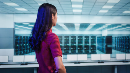 Professional woman stands overlooking modern data center filled illuminated server racks.high-tech facility represents advanced cybersecurity,cloud computing infrastructure,digital network management