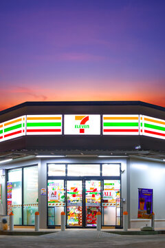 Samut Sakhon, Thailand - January 02, 2026 : 7 Eleven convenience store with illuminated logo signboard lighting on geometric polygonal flat slab roof against twilight sky in vertical frame