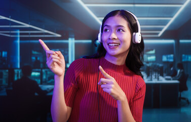 Friendly Asian customer support call center agent wears headset in high-tech control room. She provides professional online assistance and manages communications in busy digital operations center.