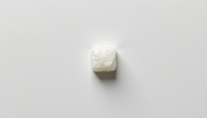 An isolated white substance, possibly sugar or salt, stands alone against a light gray background.
