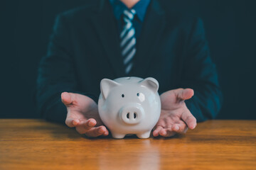 Businessman protecting piggy bank on wooden table, concept of financial security, savings protection, investment safety, wealth management, insurance, risk management, and personal finance planning.