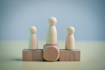 Wooden figures standing on blocks with one leader in center. Concept of leadership, teamwork, hierarchy, management, organization structure, business strategy, authority and human resources.