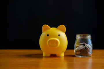 Yellow piggy bank beside a glass jar of coins on wooden table, minimal finance concept for savings, budgeting, investment growth, personal wealth, money management and smart planning.