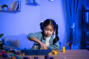 Cute Asian girl playing with wooden building blocks at night. Child learning and having fun with...
