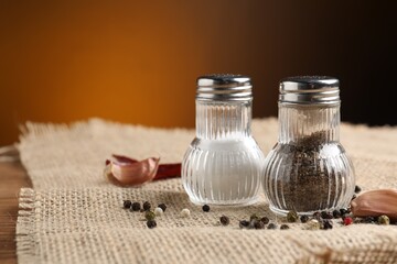 Salt and pepper shakers with spices on table against brown background, closeup. Space for text