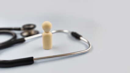 Single wooden figure beside a stethoscope symbolizing individual health, personal medical care,...