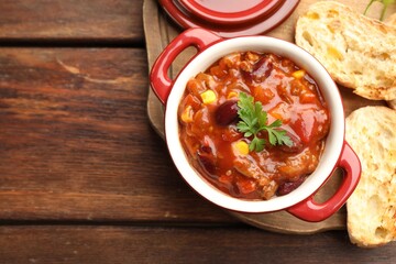 Delicious chili con carne served on wooden table, top view. Space for text