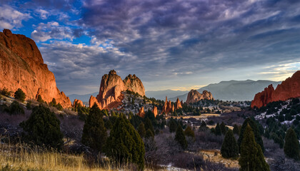 A breathtaking landscape of rugged rock formations and evergreen trees under a dramatic sky at sunrise