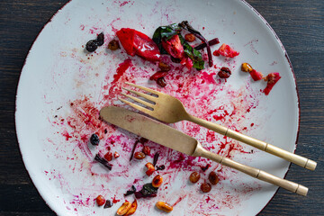 Dirty plate, fork and knife after eating on a wooden table, closeup, top view. End of meal