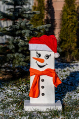 Wooden handmade snowman in a red hat and scarf against the backdrop of a winter garden, closeup. Christmas decorative ornaments as a symbol of good luck in the new year