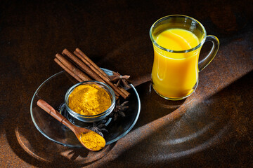 Golden milk in glass cup on wooden background at morning, alternative medicine concept. Healthy drink with turmeric, milk and spices, closeup. Turmeric latte, trendy hot healthy drink