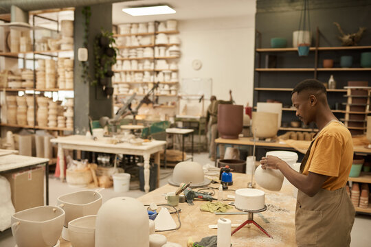 Young African ceramist working on a clay pot in a large workshop