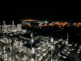 Fototapeta premium City skyline at night with many tall buildings and a large industrial area. The lights from the buildings and factories create a bright and bustling atmosphere