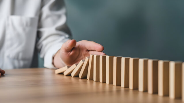 A person stopping a domino effect with their hand on a wooden table