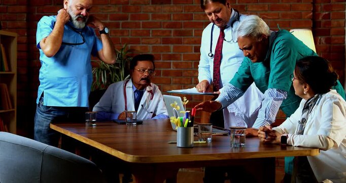 Indian confident doctors discussing case on laptop together senior surgeons and physicians reviewing digital medical records on desk in hospital while deciding proper course of action for treatment