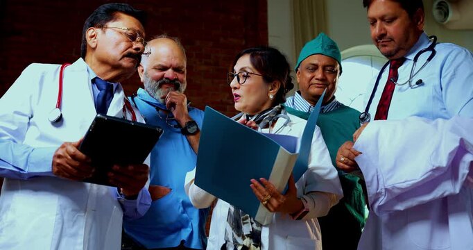 Indian confident doctors discussing case paper together senior surgeons and physicians reviewing patient chart file before operation while standing as medical team finding treatment solution