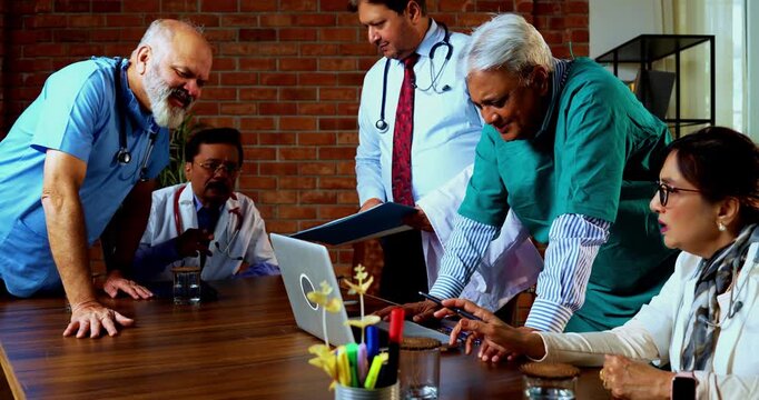 Indian confident doctors discussing case on laptop together senior surgeons and physicians reviewing digital medical records on desk in hospital while deciding proper course of action for treatment
