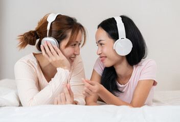 Two individuals lie on a bed, smiling and wearing headphones in a cozy indoor setting. Their relaxed posture and joyful expressions reflect connection, communication, shared enjoyment through music.