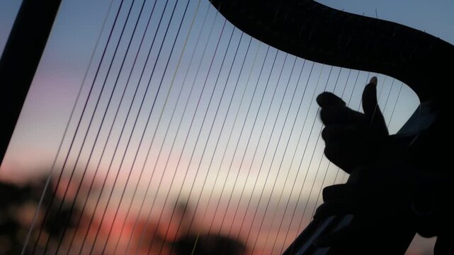 Silueta de manos de hombre tocando las cuerdas de un arpa llanera durante un atardecer colorido