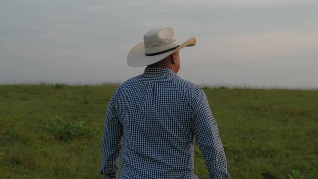 Hombre con sombrero de vaquero caminando por una llanura al amanecer, concepto de agricultura y vida rural