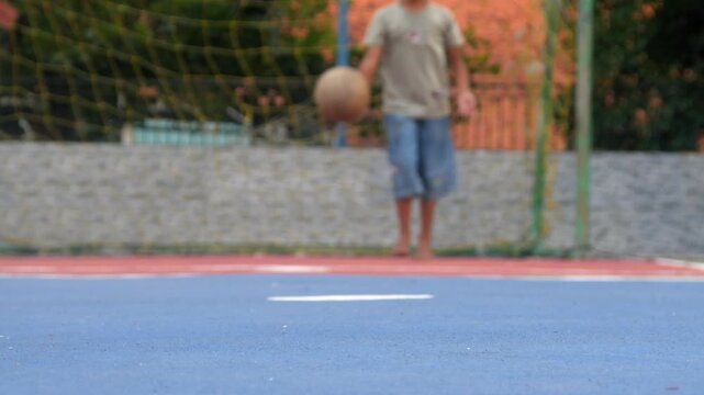 Boys playing soccer barefoot. Kicking the ball from the penalty spot into the goal on an outdoor futsal field.