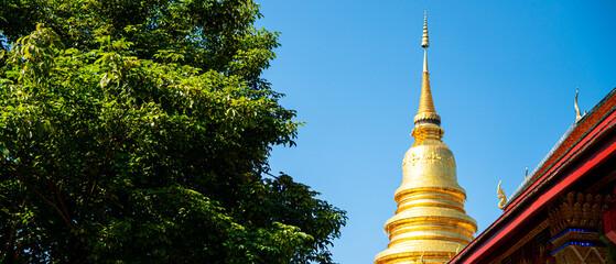 Majestic Golden Pagoda under Clear Blue Sky with Lush Green Trees, Traditional Thai Buddhist Architecture
