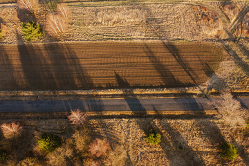 Droga przebiegająca przez r&oacute;wninę pokrytą polami uprawnymi, łąkami, kępami drzew. Jest słoneczny dzień. Zdjęcie wykonano z dużej wysokości z użyciem drona.