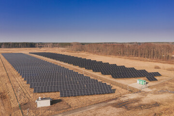 Farma paneli fotowoltaicznych na brązowym gruncie. Jest słoneczny dzień. Zdjęcie z drona.