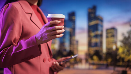 Business professional holding takeaway coffee and smartphone outdoors, modern city background, evening light urban lifestyle, mobile communication productivity work break,life balance.