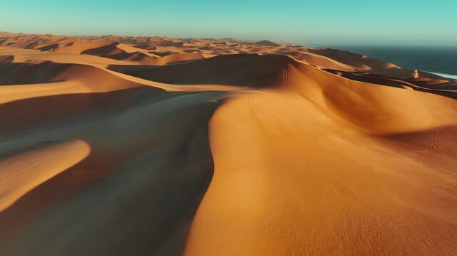 Stunning aerial drone footage of the Namib Desert where vast sand dunes meet the Atlantic Ocean. Dramatic contrast between golden dunes and deep blue water
