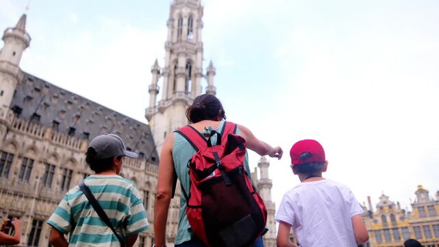Family tourists sightseeing in front of brussels town hall at grand place, mother pointing towards the impressive gothic architecture, exploring european city during summer vacation