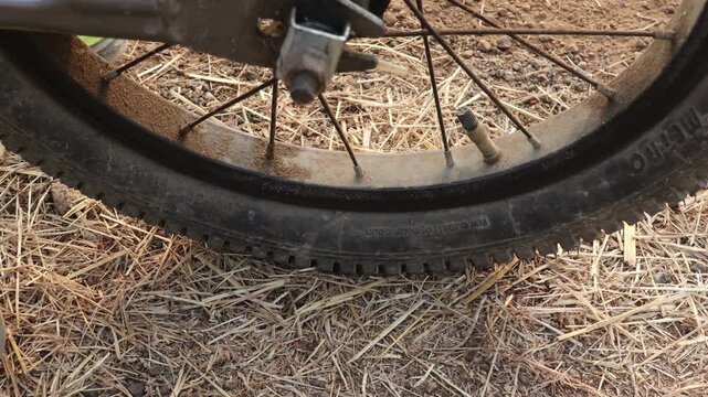 Close-up of deflated mountain bike tire with visible puncture on dry dirt trail, flat bicycle wheel stuck in rough outdoor terrain during off-road cycling adventure