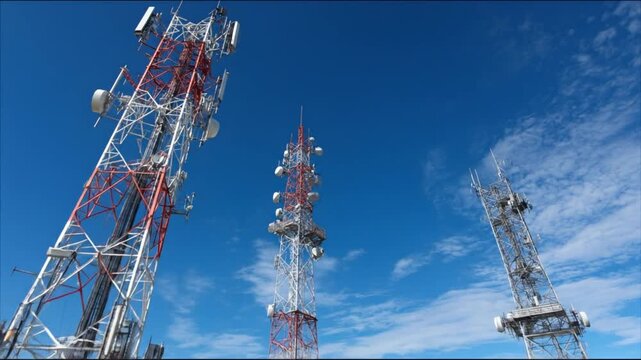 Towering lattice radio masts rise against a blue sky, with antennas, dishes, and cables above