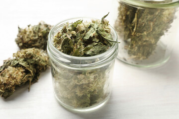 Dried medicinal herbs in jars on white wooden table, closeup